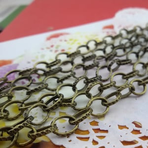 以下が含まれることがあります： 質感のある楕円形のリンクでできたチェーンのクローズアップ。チェーンは真鍮色の金属でできています。