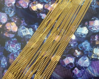 May include: Close-up of multiple strands of gold-colored chain. The chains are arranged diagonally across the frame, with a detailed, textured appearance. The background features a dark, textured surface with hints of purple and blue.