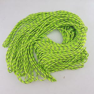 Puede incluir: Una cuerda enrollada con un patrón moteado verde neón y gris. La cuerda está enrollada firmemente en forma circular, con algunos hilos que se extienden hacia afuera. La cuerda parece estar hecha de un material duradero.