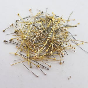 May include: A pile of mixed metal head pins with gold, silver, and bronze colored heads. The pins are about 1 inch long.