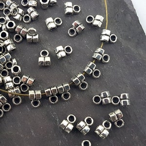 May include: Silver-toned metal bead caps with two loops on each end. The bead caps are scattered on a dark grey surface.