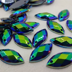 Puede incluir: Un conjunto de pedrería iridiscente en forma de marquesa. Las gemas presentan un diseño facetado con un efecto de cambio de color, mostrando tonos de verde, azul y morado. Cada piedra tiene un pequeño agujero en un extremo, para adornar.