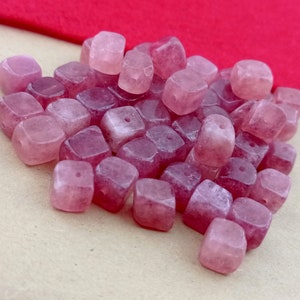 May include: A pile of pink and white square-shaped gemstone beads. The beads are translucent and have a slight shimmer.