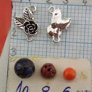 May include: Two silver metal charms, one with a rose and leaves, the other with a bird design. Three beads, one blue, one red, and one orange, with measurements in millimeters: 10 mm, 8 mm, and 6 mm.
