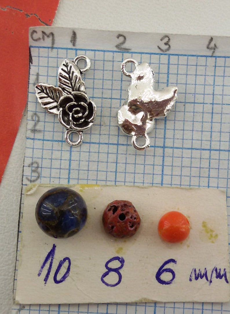 May include: Two silver metal charms, one with a rose and leaves, the other with a bird design. Three beads, one blue, one red, and one orange, with measurements in millimeters: 10 mm, 8 mm, and 6 mm.