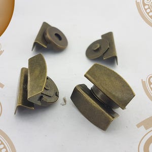 Puede incluir: Cuatro cierres magnéticos de latón antiguo. Cada cierre consta de dos piezas: una pieza curva y rectangular y una pieza circular. Los cierres están diseñados para su uso en bolsos, carteras u otros proyectos de artesanía.