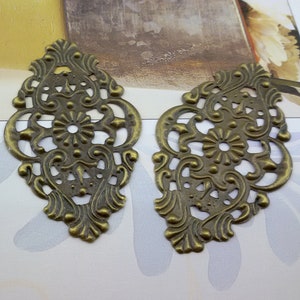 May include: Two ornate metal embellishments with a filigree design in a bronze finish. The embellishments are shaped like a teardrop and have a detailed floral pattern.