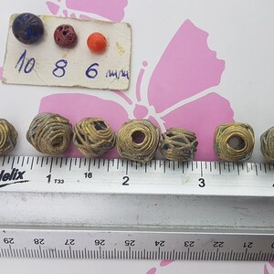 May include: Eight gold wire wrapped beads, each approximately 1 inch in diameter, are lined up on a ruler. The ruler is marked in inches and 1/16ths of an inch. A small card with the numbers 10, 8, and 6 is visible in the background.