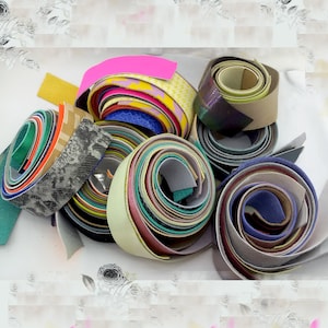 May include: A collection of colorful leather strips rolled up in various sizes and patterns. The strips are made of different colors, including pink, yellow, blue, green, and brown.