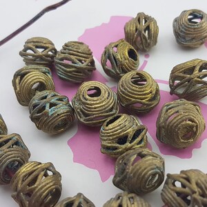 May include: A collection of 17 brass beads with a wire cage design. The beads are a mix of gold and green tones.