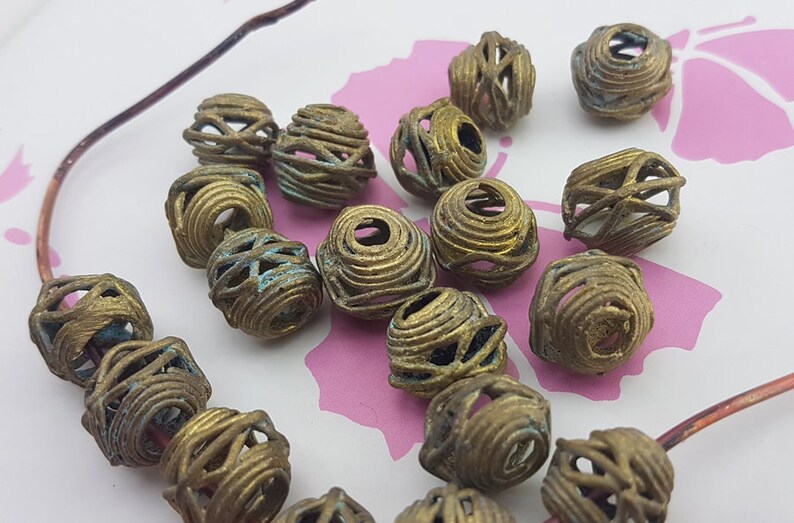 May include: A collection of 17 brass beads with a wire cage design. The beads are a mix of gold and green tones.