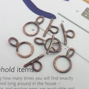 May include: A collection of eight copper-toned metal findings in various shapes and sizes. Some have a ring shape, while others have a bar shape. These findings are ideal for jewellery making or other craft projects.