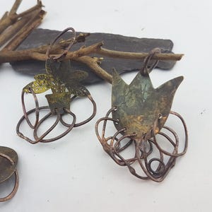 Könnte beinhalten: Ein Paar handgefertigte Ohrringe mit einem Blattpflanzen- und Tulpendesign. Die Ohrringe sind aus Kupferdraht gefertigt und haben eine rustikale, oxidierte Oberfläche.