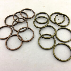 Könnte beinhalten: Eine Ansammlung von kreisförmigen Metallspaltringen, die in zwei Gruppen angeordnet sind. Die linke Gruppe besteht aus kupferfarbenen Ringen, während die rechte Gruppe antik messingfarbene Ringe enthält. Jeder Ring besteht aus einem Draht.