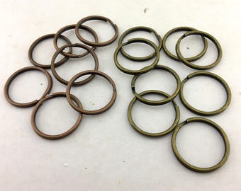 May include: A collection of circular metal split rings arranged in two groups. The left group consists of copper-toned rings, while the right group features antique brass-toned rings. Each ring is made of a single coiled wire with an overlapping end.