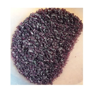 May include: A close-up of a bowl filled with small, iridescent purple glass pieces. The glass pieces are irregular in shape and have a shiny, reflective surface.