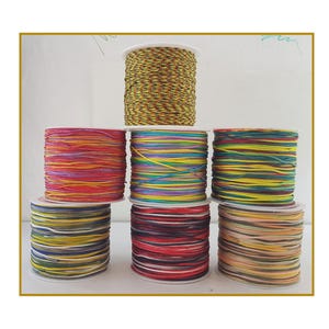 May include: A selection of colourful cord spools, tightly wound on white cores. The cords feature a variety of colours, including red, yellow, green, blue, and purple. The spools are stacked, displaying the diverse colour palette and textures.