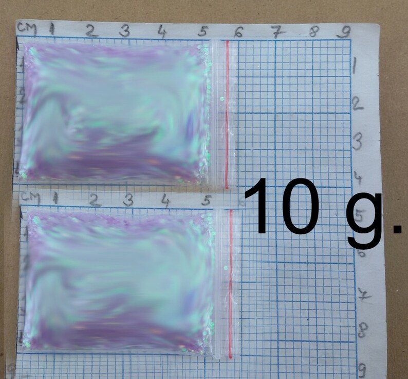 以下が含まれることがあります： 虹色のグリッターが詰まった透明な小さなプラスチック袋2つ。各袋には10グラムのグリッターが入っています。袋はグリッド状の表面に置かれています。