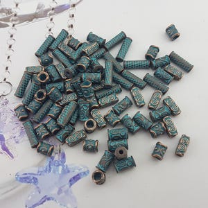 May include: A large pile of teal blue and copper coloured beads with intricate designs. The beads are cylindrical in shape and have a slightly textured surface.