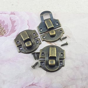 May include: Three antique brass box clasps with two screws. Each clasp has a hinged lid and a latch.