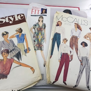 Pode incluir: Três padrões de costura para roupas. O primeiro padrão é para um vestido com estampa floral. O segundo padrão é para uma blusa e calças. O terceiro padrão é para uma blusa e calças com estampa xadrez. Os padrões são da McCall's e Today's Fit.