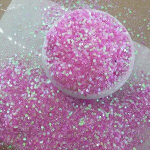 以下が含まれることがあります： 虹色のピンクのグリッターのクローズアップ。白い皿に少量のグリッターが入っています。