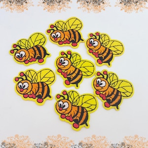May include: Embroidered bee patches. Each patch features a cartoon bee with yellow wings, orange and black striped body, and red accents. The patches are arranged on a white background.