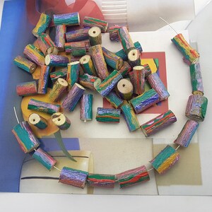 May include: A selection of colourful wooden beads, some strung together to form a necklace. The beads are cylindrical, painted with streaks of blue, green, red, and yellow. Some beads are scattered, while others are connected by a thin wire.