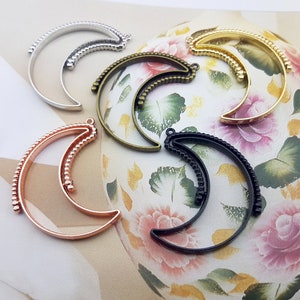May include: Five crescent moon shaped metal frames in different colors. The frames are silver, gold, copper, and black. The frames are all the same size and have a beaded edge.