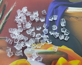 May include: A large quantity of clear plastic earring backs in a flower shape. The backs are scattered on a colourful surface.
