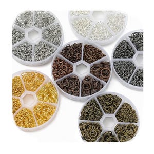 May include: A selection of jump rings in diverse metallic colours, such as silver, gold, bronze, and gunmetal. The jump rings are arranged in clear, segmented containers, suitable for jewellery making and craft projects.