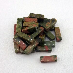 May include: A pile of green, red, and brown rectangular gemstone beads. The beads are smooth and polished.