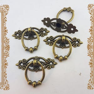 May include: Vintage-style brass drawer pulls with intricate patterns. The pulls have ring handles and decorative backplates. These antique-style handles are suitable for cabinets or furniture restoration projects, adding a touch of elegance.
