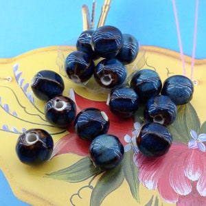 May include: A collection of dark blue ceramic beads with brown and white accents. The beads are arranged on a yellow surface with a floral design.
