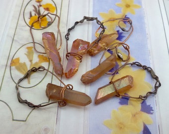 May include: A copper wire necklace with five iridescent orange quartz crystals. The crystals are wrapped in wire and hang from a twisted copper chain.