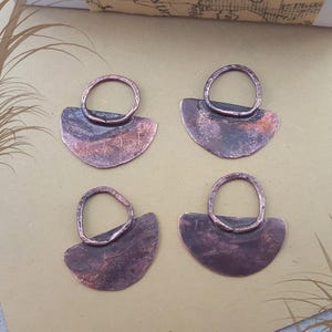 Peut inclure: Quatre pendentifs en cuivre faits à la main, en forme de demi-lune avec une boucle circulaire. Les pendentifs présentent un aspect rustique et vieilli avec des variations de couleur allant du brun foncé au brun rougeâtre.