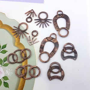 May include: Assortment of copper-toned metal jewelry findings, including rings, hoops, and pendants. The findings are in various shapes and sizes, with some featuring a textured finish.