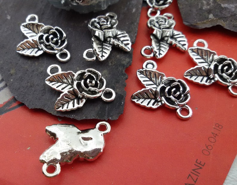 May include: Silver tone metal rose flower charms with two jump rings. The charms feature a rose with leaves and are perfect for jewelry making.