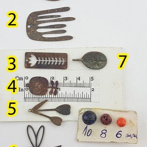 May include: A collection of small, antique-style metal charms and beads. The charms include leaf, comb, and dragonfly shapes, along with a flower and a leaf-shaped charm. There are also three small beads in blue, red, and orange.
