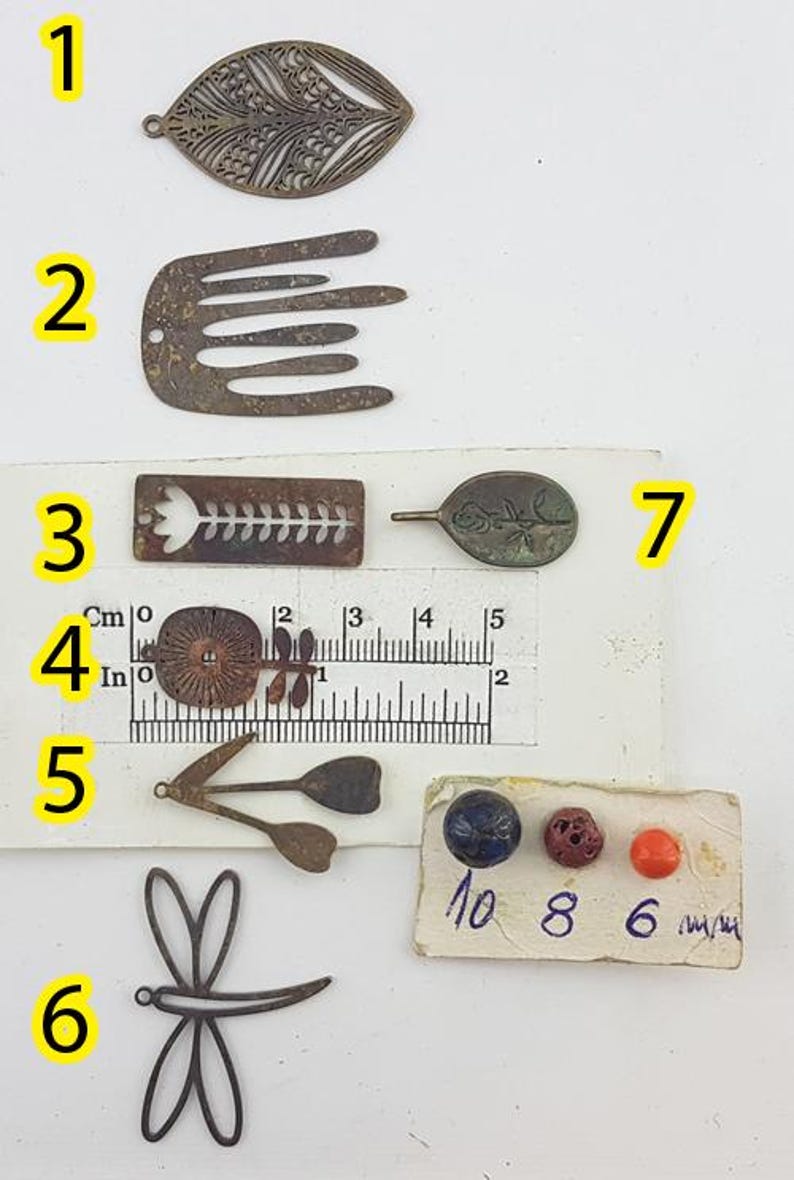 May include: A collection of small, antique-style metal charms and beads. The charms include leaf, comb, and dragonfly shapes, along with a flower and a leaf-shaped charm. There are also three small beads in blue, red, and orange.