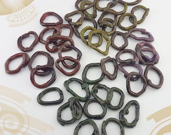 May include: A collection of small, irregularly shaped rings in various colors, including shades of brown, green, and purple. The rings appear to be made of a textured material and are scattered across a light-colored surface. The overall aesthetic suggests a craft or jewelry-making theme.