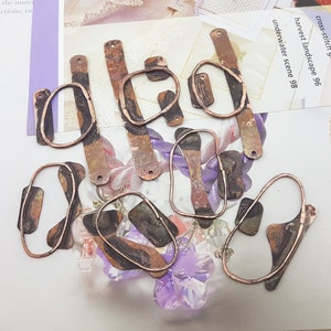 May include: Assortment of eight copper-toned metal jewellery findings with irregular shapes and a textured finish. The findings are in various sizes and shapes, including ovals, rectangles, and free-form shapes.