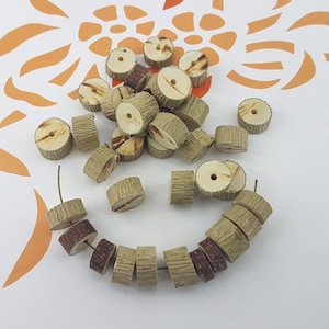 Op de afbeelding: Een stapel natuurlijke houten kralen met een gat in het midden. De kralen zijn lichtbruin en hebben een ruwe textuur. Sommige van de kralen zijn in een cirkel op een wit oppervlak gerangschikt.