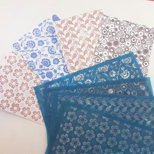 May include: A selection of patterned paper sheets in diverse designs and colours. The sheets display floral, leaf, and geometric patterns in shades of blue, brown, and white. Some sheets are stencils with detailed floral designs.