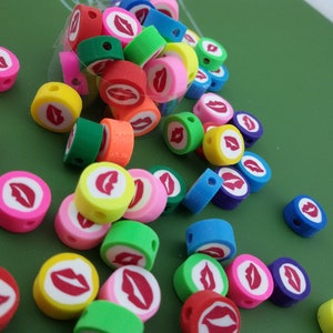 May include: A collection of colorful round beads with a red lip design. The beads are made of polymer clay and have a hole in the center for stringing.