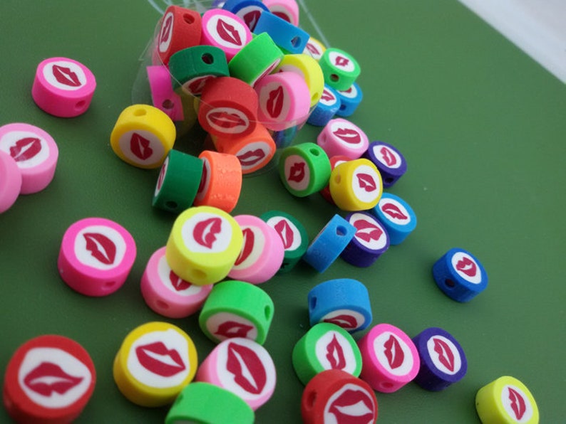 May include: A collection of colorful round beads with a red lip design. The beads are made of polymer clay and have a hole in the center for stringing.