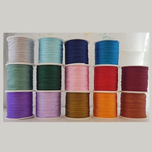 May include: A selection of colourful cord spools in shades of blue, green, pink, red, and purple. The cords are neatly wound on white spools, providing a variety of options for crafts and jewellery making. The cords are arranged in a neat, organised display.