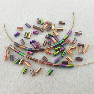 May include: A collection of iridescent brown and clear glass seed beads, some strung on thin wire. The beads are cylindrical in shape and have a metallic sheen.