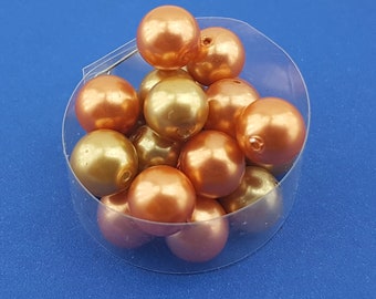 May include: A close-up of a pile of round, pearlescent beads in shades of gold and peach. The beads are arranged in a clear plastic container.