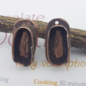 May include: Two oval-shaped copper pendant blanks with a hole at the top. The blanks are dark brown with a copper patina and have a smooth, slightly textured surface.